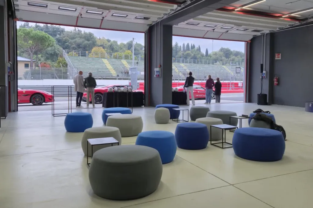 Box del circuito allestito a lounge con pouf e tavolini, portoni aperti sulla pit lane