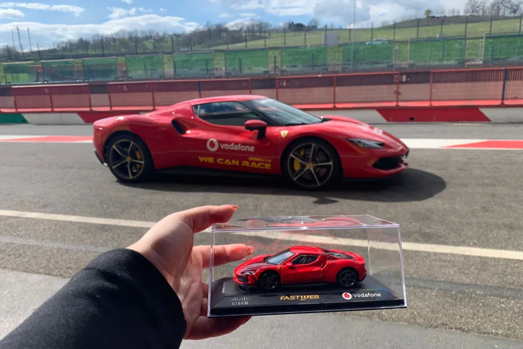 Modellino in scala della supercar brandizzata consegnato ai partecipanti, con la vettura reale in pista alle spalle